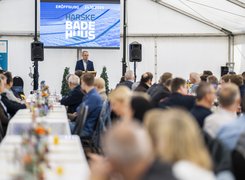 Das Bild zeigt ein Festzelt von innen. Ein Mann hält eine Rede vor einem Bildschirm.