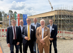 Auf dem Bild sind sechs Männer vor einer Baustelle erkennbar. Im Hintergrund befindet sich die zu sanierende Einrichtung.