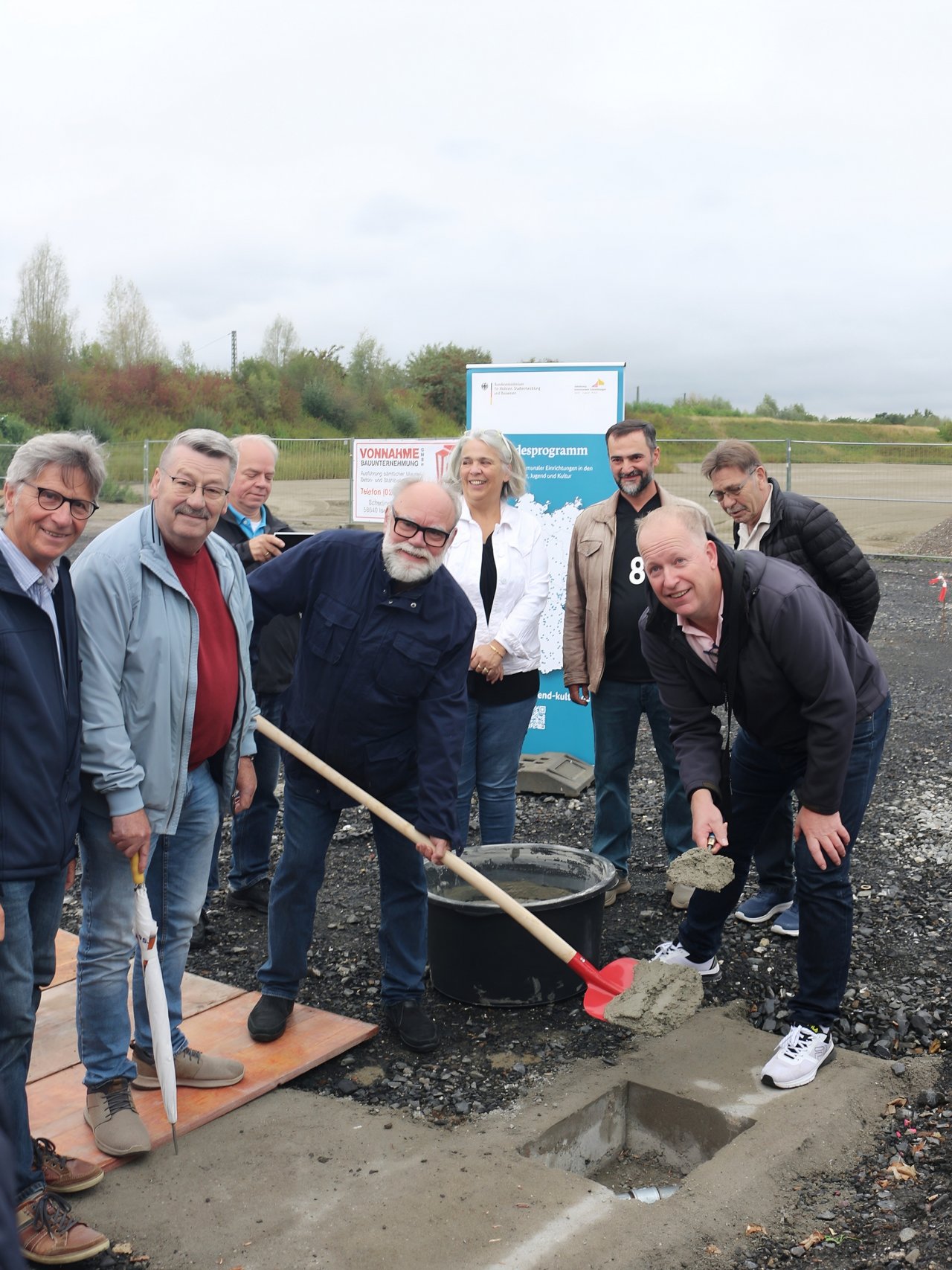 Quelle: Elina Schulze, Gemeinde Bönen Das Bild zeigt mehrere Personen um einen Betonschacht gruppiert. Eine von ihnen schaufelt frischen Beton in die Öffnung des Schachts.