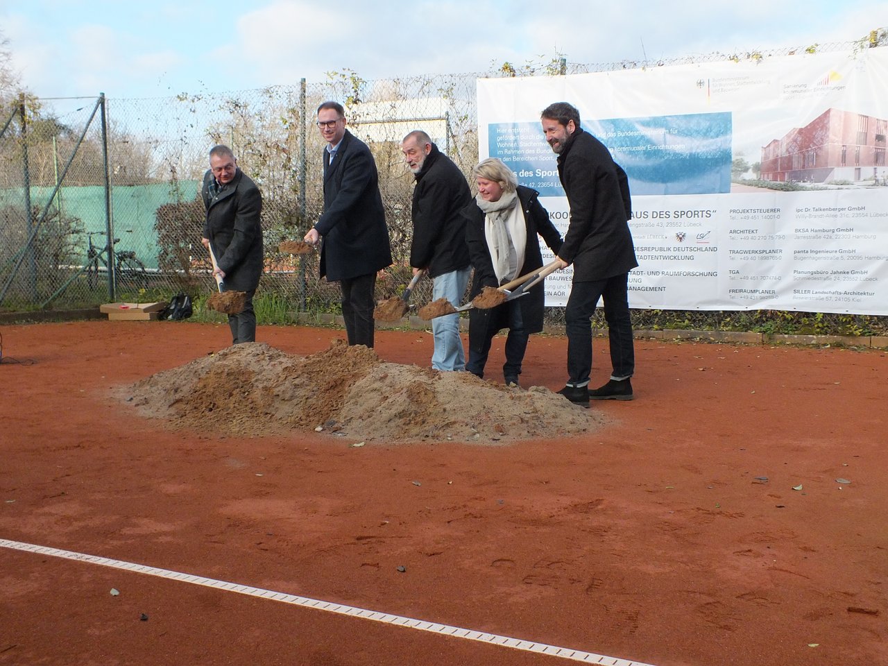 k.A. Das Bild zeigt fünf Personen, die einen Spatenstich begehen, indem sie Erde mit einem Spaten aufheben.