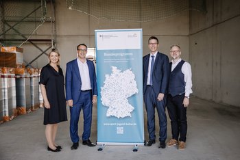 Das Bild zeigt vier Personen, die um ein Roll-Up versammelt stehen und in die Kamera blicken.