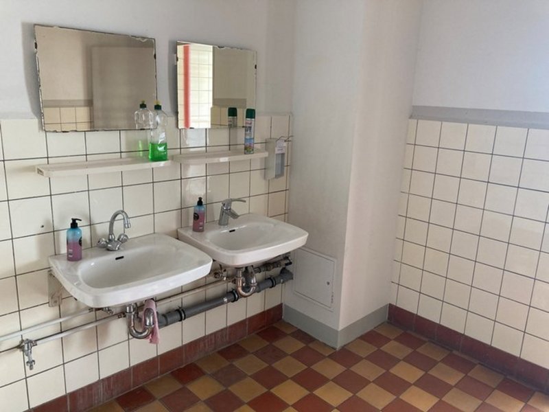 Das Bild zeigt zwei Waschbecken mit Ablage und Spiegel in einem gefliesten Sanitärraum.