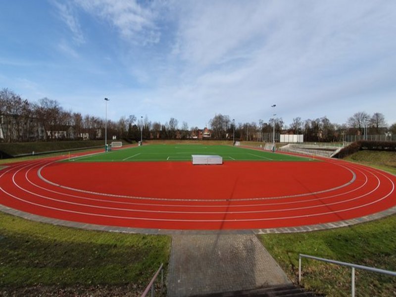 Das Bild zeigt einen Fußballplatz mit roter Laufbahn außen herum.