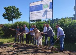 © Stadt Alfeld (Leine) – Hochbauamt Man sieht Menschen vor einem Bauschild, die einen Spatenstich vornehmen.