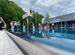 LBB GmbH / Stadt Leichlingen Der Bürgermeister Das Bild zeigt mehrere Personen, die vor dem Schwimmbecken stehen. Eine Person befindet sich mit verschränktem Armen auf einem Sprungbrett.