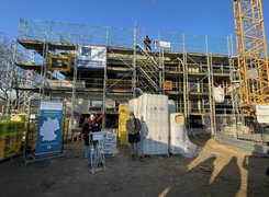 Foto: Mario Kampermann Man sieht zwei Menschen vor einem eingerüsteten Gebäude auf einer Baustelle. Sie halten eine Rede.