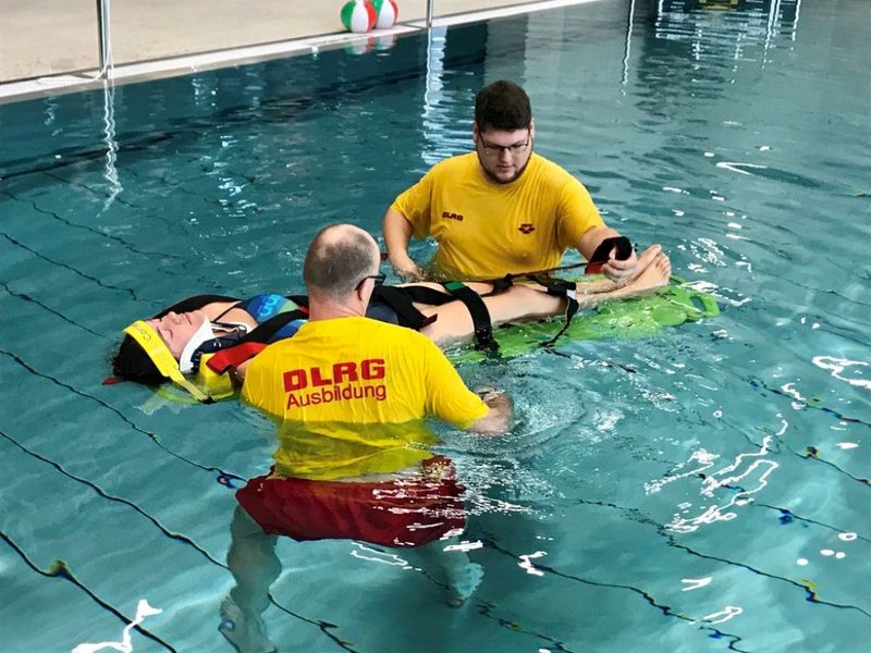 Das Bild zeigt zwei Männer in gelben DLRG-T-Shirts, die im Wasser eine dritte Person retten.