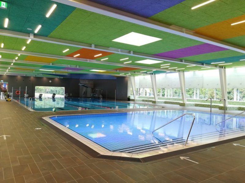 Das Bild zeigt zwei separate Schwimmbecken in einem modernen, bunt gestalteten Hallenbad.