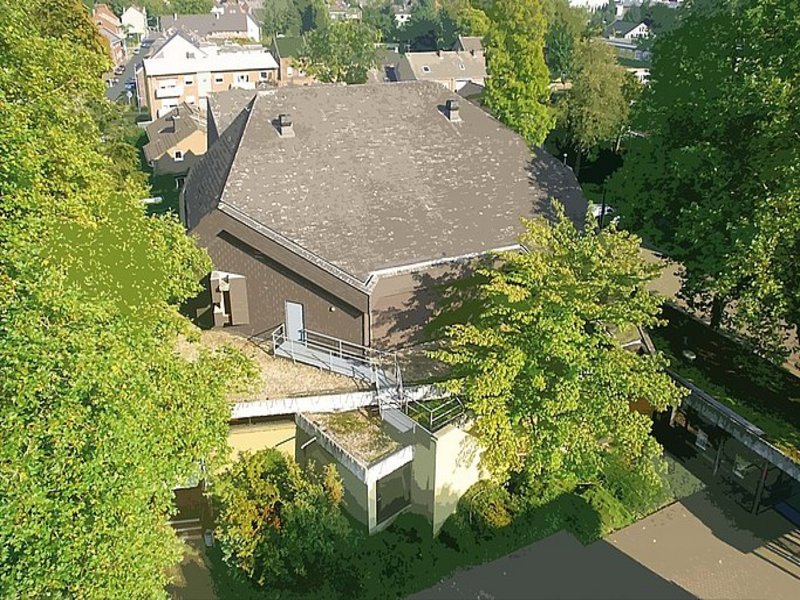 Das Bild zeigt ein Gebäude mit dunklem Dach aus der Luftperspektive.