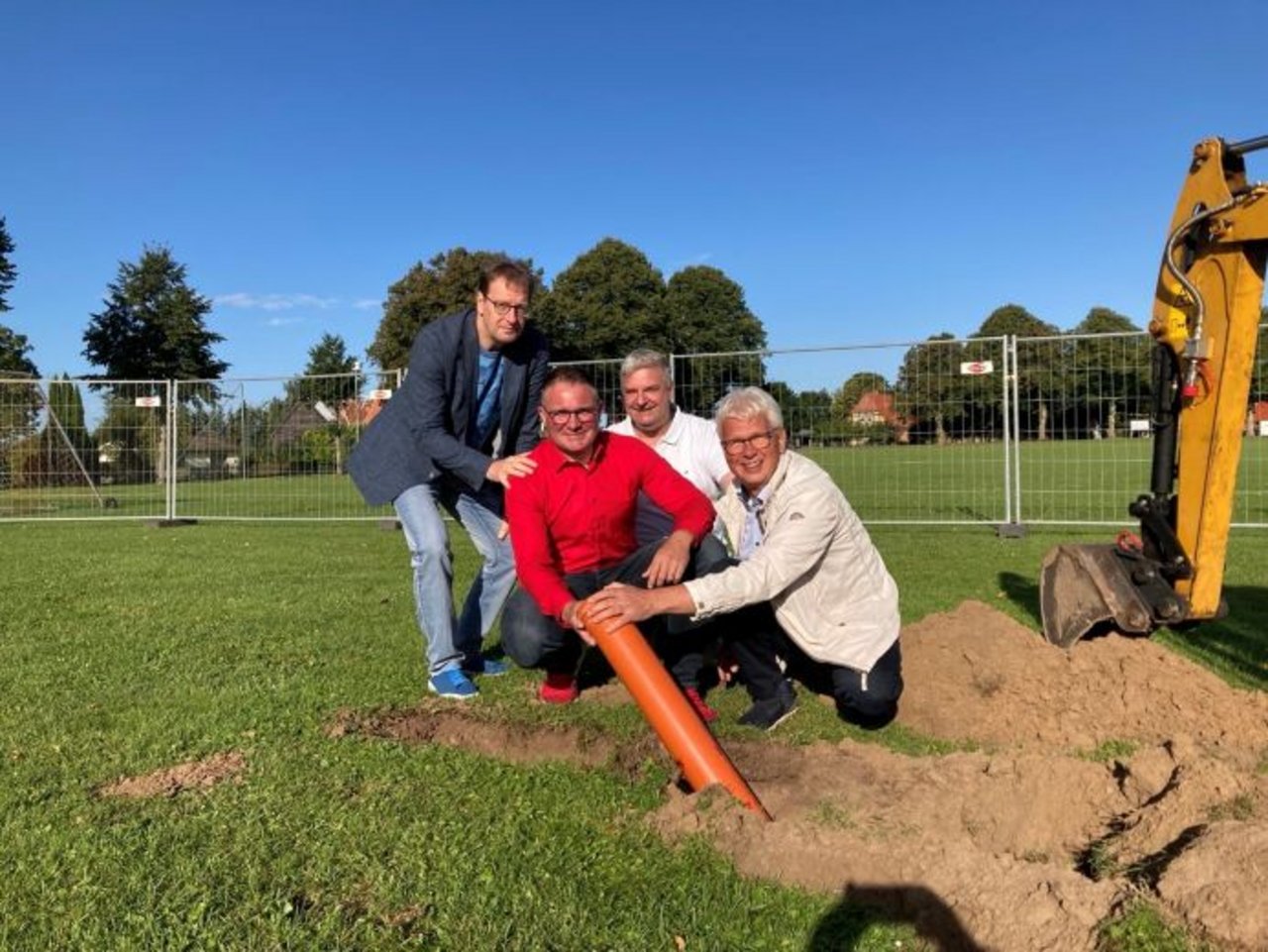 Quelle: C. Brinkhoff, Spatenstich Dat Dörp, 12.09.2025 Man sieht vier Männer auf einer Wiese, die ein Rohr in den Boden legen.