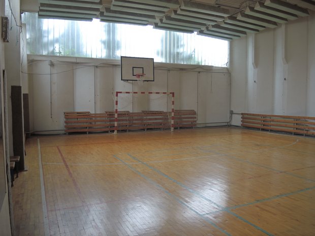 Innenraum einer Turnhallt mit braunem Boden und Basketballkorb und Tor.