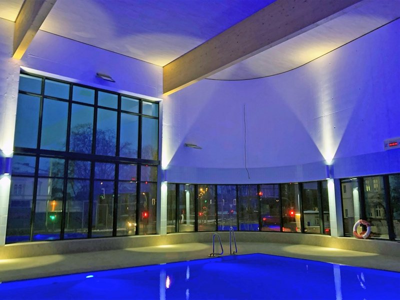 Das Bild zeigt ein beleuchtetes Schwimmbecken in einem Hallenbad mit Fensterfront bei Nacht