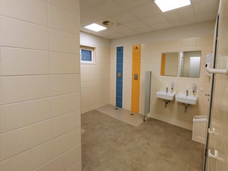 Das Bild zeigt einen Sanitärbereich mit zwei Duschen und zwei Waschbecken mit Spiegeln.