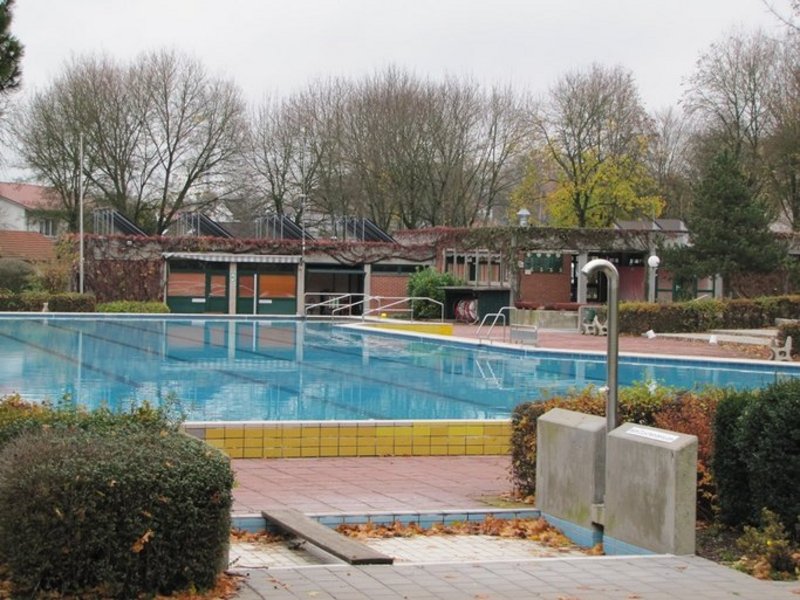 Das Bild zeigt ein Schwimmbecken in einem Freibad, im Vordergrund ist ein Fußbecken mit Dusche zu sehen.