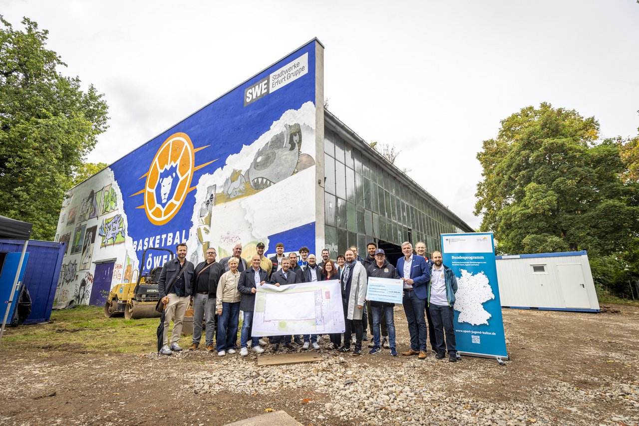 Das Bild zeigt eine Gruppe von Menschen, die vor einer Baustelle stehen und ein Banner hochhalten.
