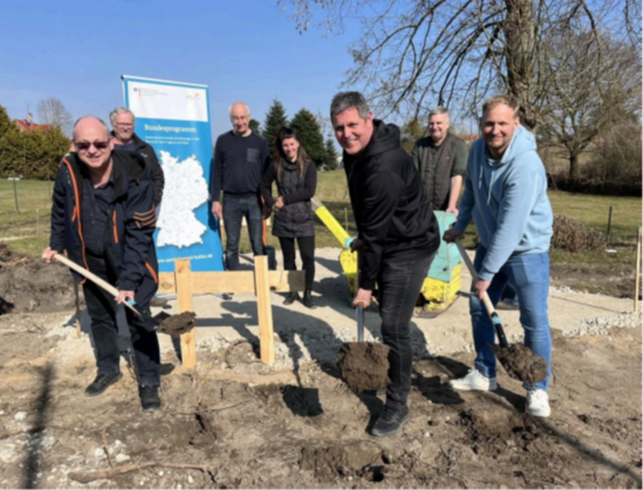 Das Bild zeigt Menschen beim symbolischen Baustart mit Spaten in der Hand.