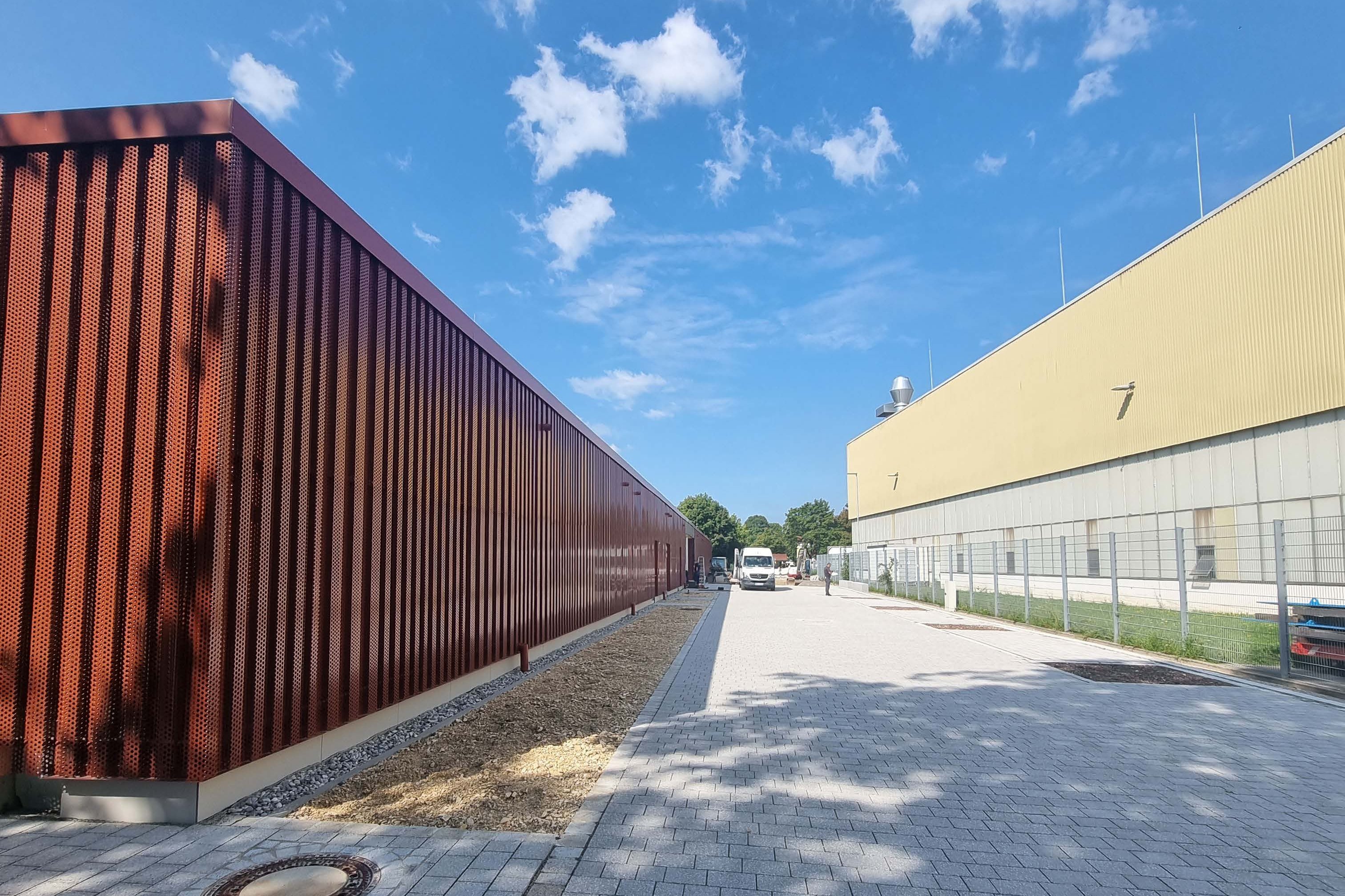 Das Bild zeigt einen gepflasterten Weg zwischen einem rotbraunen Gebäude links und einem gelben Gebäude rechts.