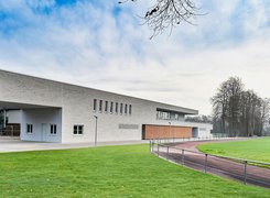 Das Bild zeigt einen Rasenplatz  mit Laufbahn und einem neuen Gebäude.