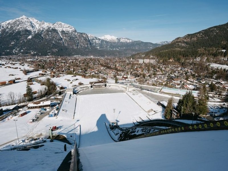 Das Bild zeigt den Blick einen schneebedeckten Skisprunghangs hinunter in ein Stadion hinein.