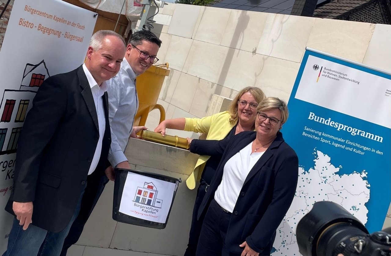 Quelle: Bürgerstiftung Kapellen an der Fleuth Das Bild zeigt zwei Frauen und zwei Männer stehend um eine Zeitkapsel. Die goldene Zeitkapsel befindet sich in der Mitte der Frontalaufnahme.
