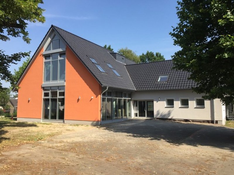 Das Bild zeigt ein modernes Gebäude mit orangen und weißen Wänden und grauem Dach.