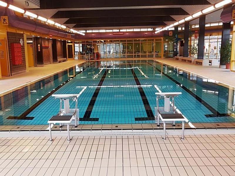 Das Bild zeigt ein Schwimmbecken in einem Hallenbad, im Vordergrund sind Startblöcke zu sehen.