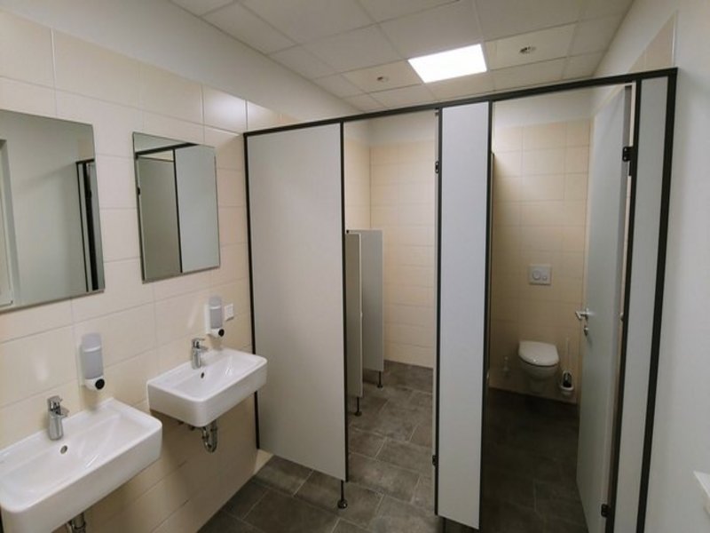 Das Bild zeigt zwei Toilettenkabinen und zwei Waschbecken mit Spiegeln.