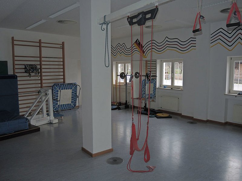 Das Bild zeigt einen in die Jahre gekommenen Fitnessraum mit unterschiedlichen Geräten.