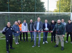 Quelle: Wallfahrtsstadt Werl, Stakemeier Elf Personen stehen in einer Reihe vor einem weißen Fußballtor. Zwei Personen spannen ein rotes Band horizontal. Ein Mann schneidet das Band in der Mitte durch.