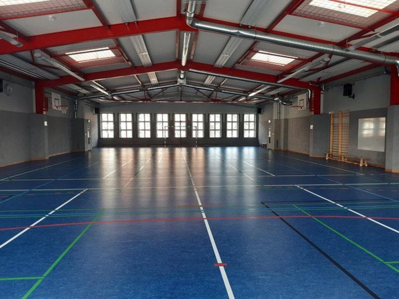 Das Bild zeigt eine Sporthalle mit blauem Boden und bunten Markierungen.