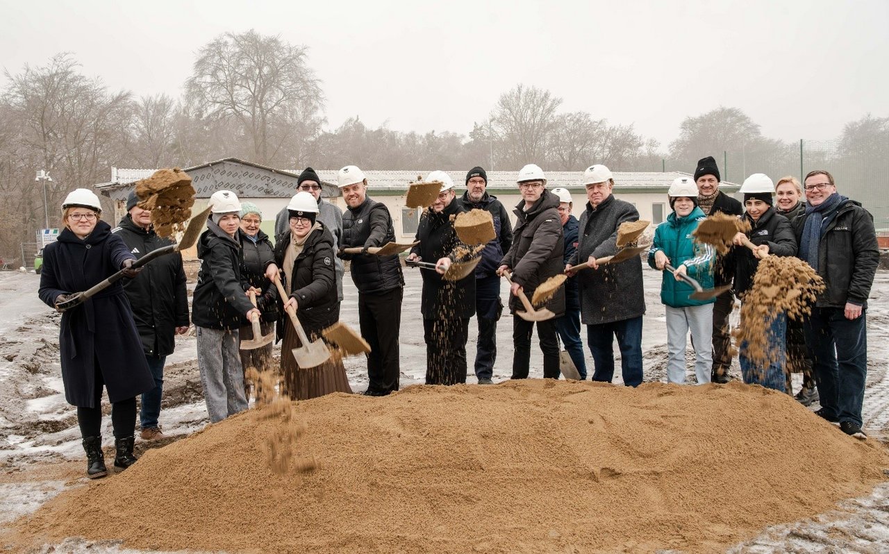 Stadt Eberswalde / Markus Mirschel Eine Gruppe von Menschen mit Bauhelmen steht hinter einem Sandhügel und wirft Erde mit Spaten in die Luft.