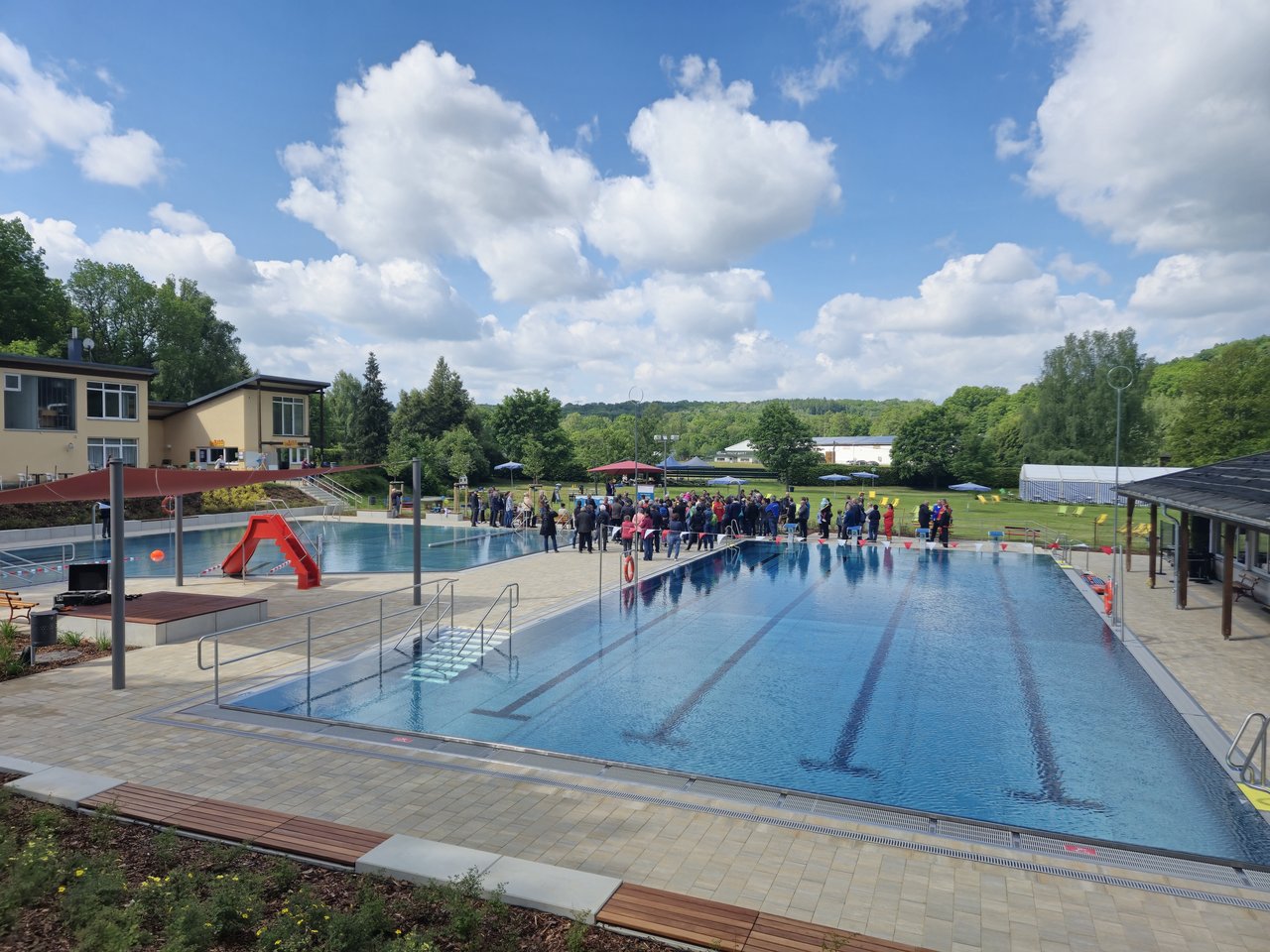 Das Bild zeigt ein Freibad, wo sich eine Gruppe von Menschen versammelt hat.