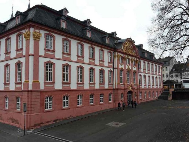 Das Bild zeigt ein Gebäude mit einer historisch anmutenden Fassade in weiß und rosé, sie enthält goldene Zierelemente - Detailperspektive.