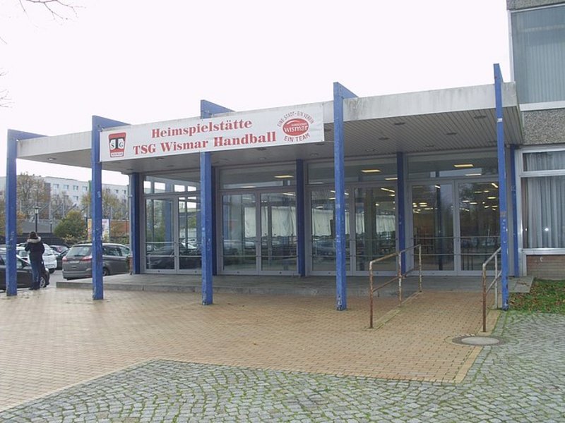 Das Bild zeigt den Eingang zu einem Gebäude mit einem Schild, das die Aufschrift Heimspielstätte TSG Wismar Handball trägt.