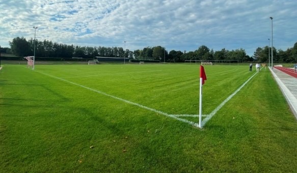 Das Bild zeigt einen grünen, saftigen Fußballrasen unter strahlend blauem Tageshimmel.