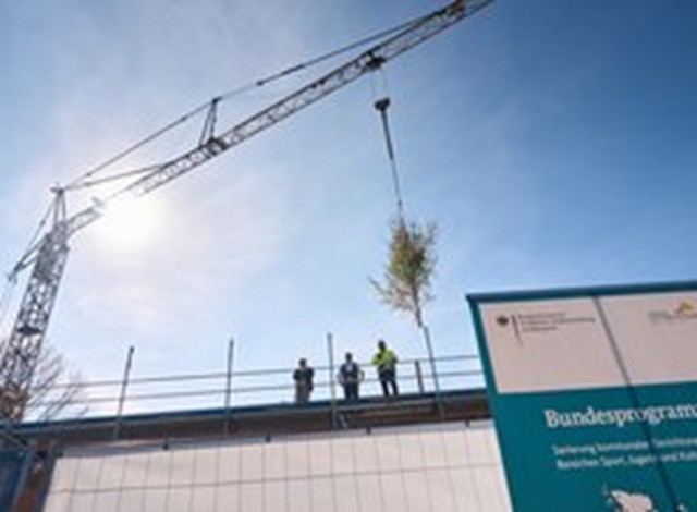 Das Bild zeigt 3 Personen in der Höhe die auf einem Baugerüst stehen, im Hintergrund sieht man einen Baukran