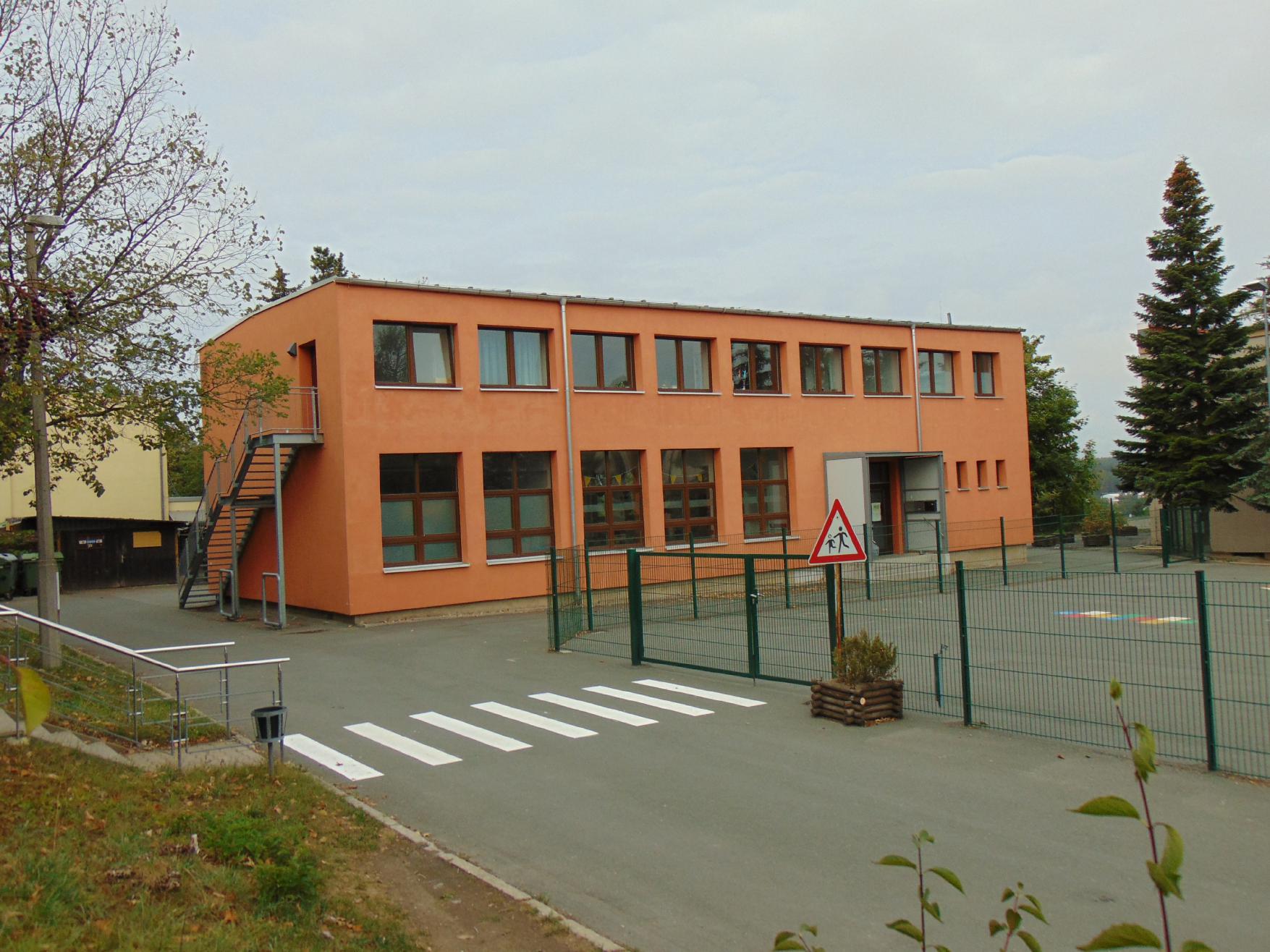 Das Bild zeigt ein oranges Gebäude, umgeben von Grünflächen.