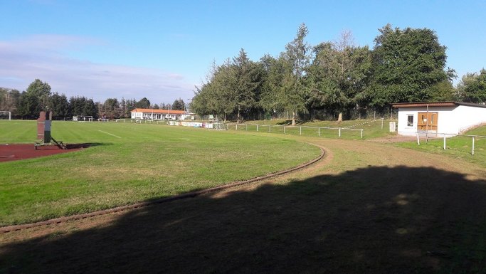Das Bild zeigt eine Rasensportfläche mit umliegender Erdlaufbahn.