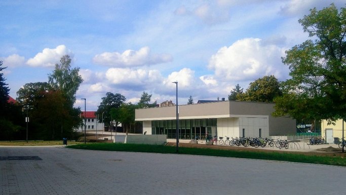 Das Bild zeigt ein modernes Einzelgebäude mit Flachdach und Fensterfront, im Vordergrund sind Räder an Abstellplätzen zu sehen.