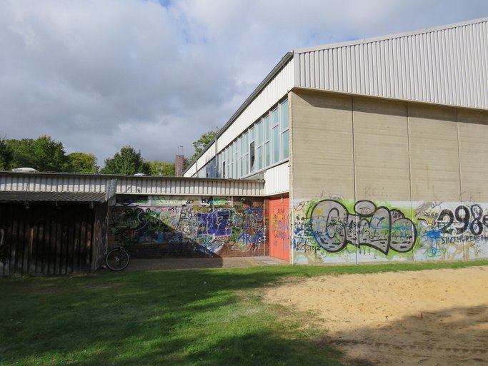 Das Bild zeigt ein Sporthallengebäude mit Graffitis an den Wänden.