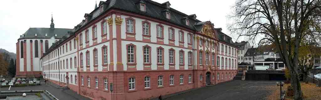 Das Bild zeigt ein Gebäude mit einer historisch anmutenden Fassade in weiß und rosé, sie enthält goldene Zierelemente - Eckperspektive