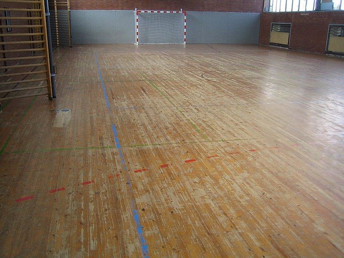 Das Bild zeigt eine Turnhalle von innen mit deutlichen Abnutzungsspuren des Holzbodens.