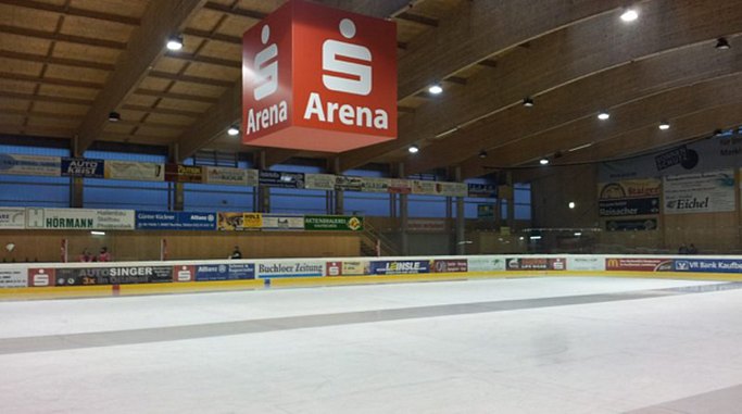 Das Bild zeigt ein Eisstadion mit Eisfläche von innen. Ein großer roter Würfel mit einem Sparkassenlogo und der Aufschrift "Arena" hängt von der Holzdecke. Die Eisfläche ist von Banden mit Werbebannern umzäunt. Die Außenwand ist mit Fensterfronten versehen.