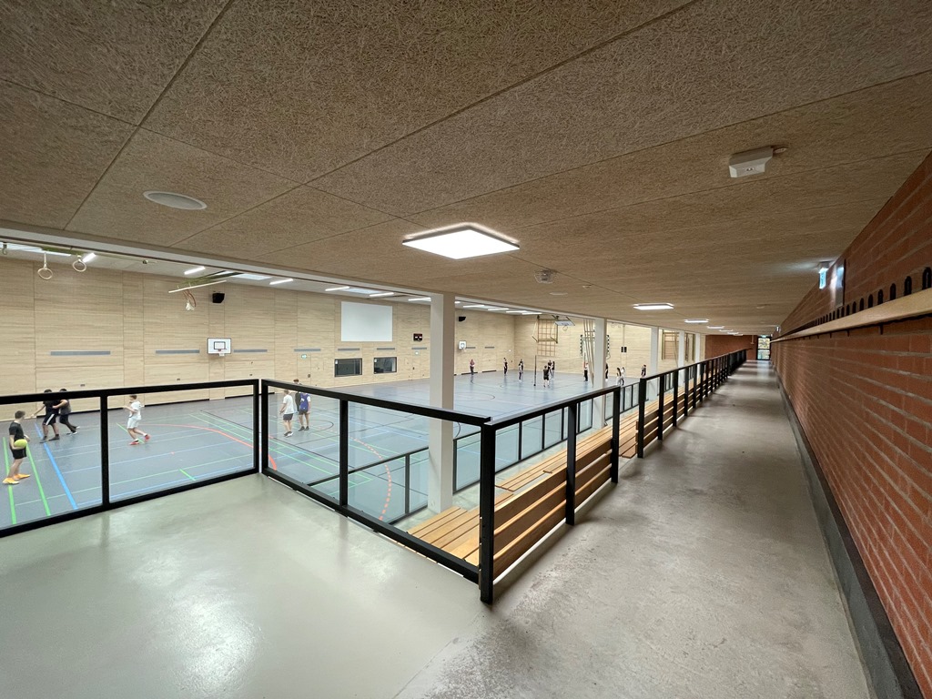 Das Bild zeigt eine Sporthalle von innen, im Vordergrund ist eine Tribüne mit Holzbänken zu sehen.