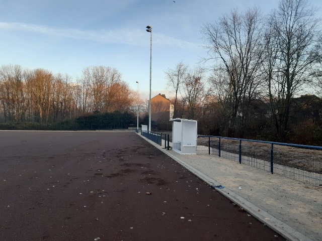 Das Bild zeigt einen Sportplatz mit Wechselhäuschen, an dem ein Weg entlang führt.