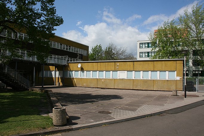 Das Bild zeigt den Anbau an ein Gebäude mit einem Vorplatz aus Betonplatten.