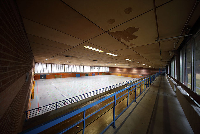 Das Bild zeigt eine in die Jahre gekommene Sporthalle aus der Perspektive der Zuschauertribüne.