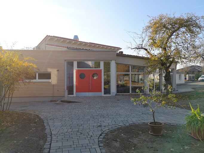 Das Bild zeigt ein modernes Gebäude mit Holzverkleidung und roter Tür.