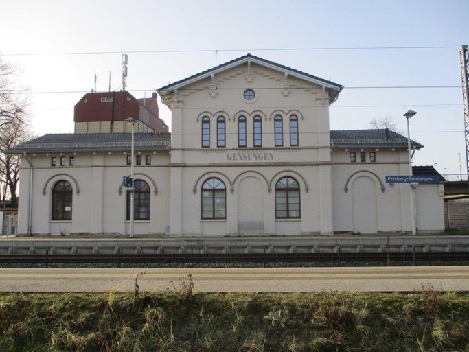 Das Bild zeigt ein historisch anmutendes Bahnhofsgebäude mit dem Schriftzug Gensungen, im Vordergrund ist ein Bahngleis zu sehen.