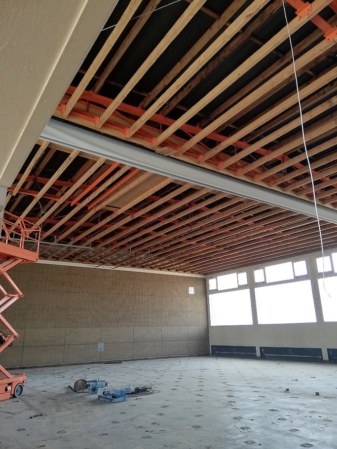 Das Bild zeigt die Sanierungsarbeiten in einer Turnhalle. Die Decke ist offen und der Hallenboden abgetragen.